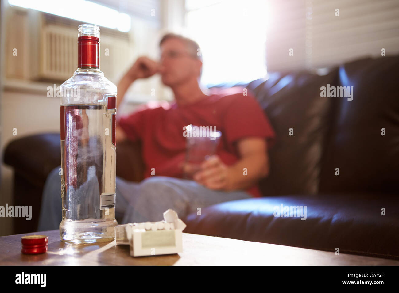 Mann sitzt auf dem Sofa mit Flasche Wodka und Zigaretten Stockfoto