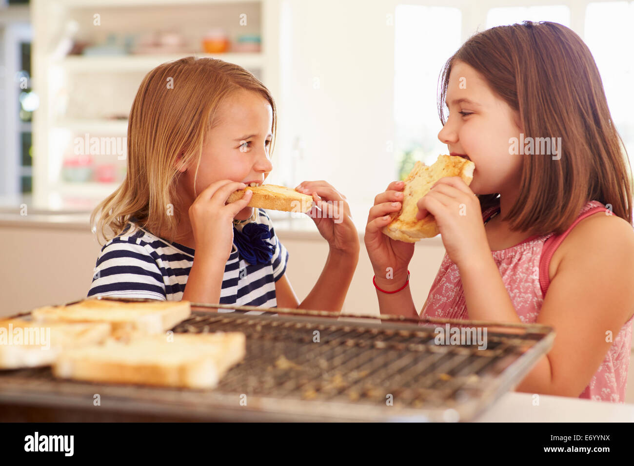 Zwei Mädchen essen Käse auf Toast In Küche Stockfoto