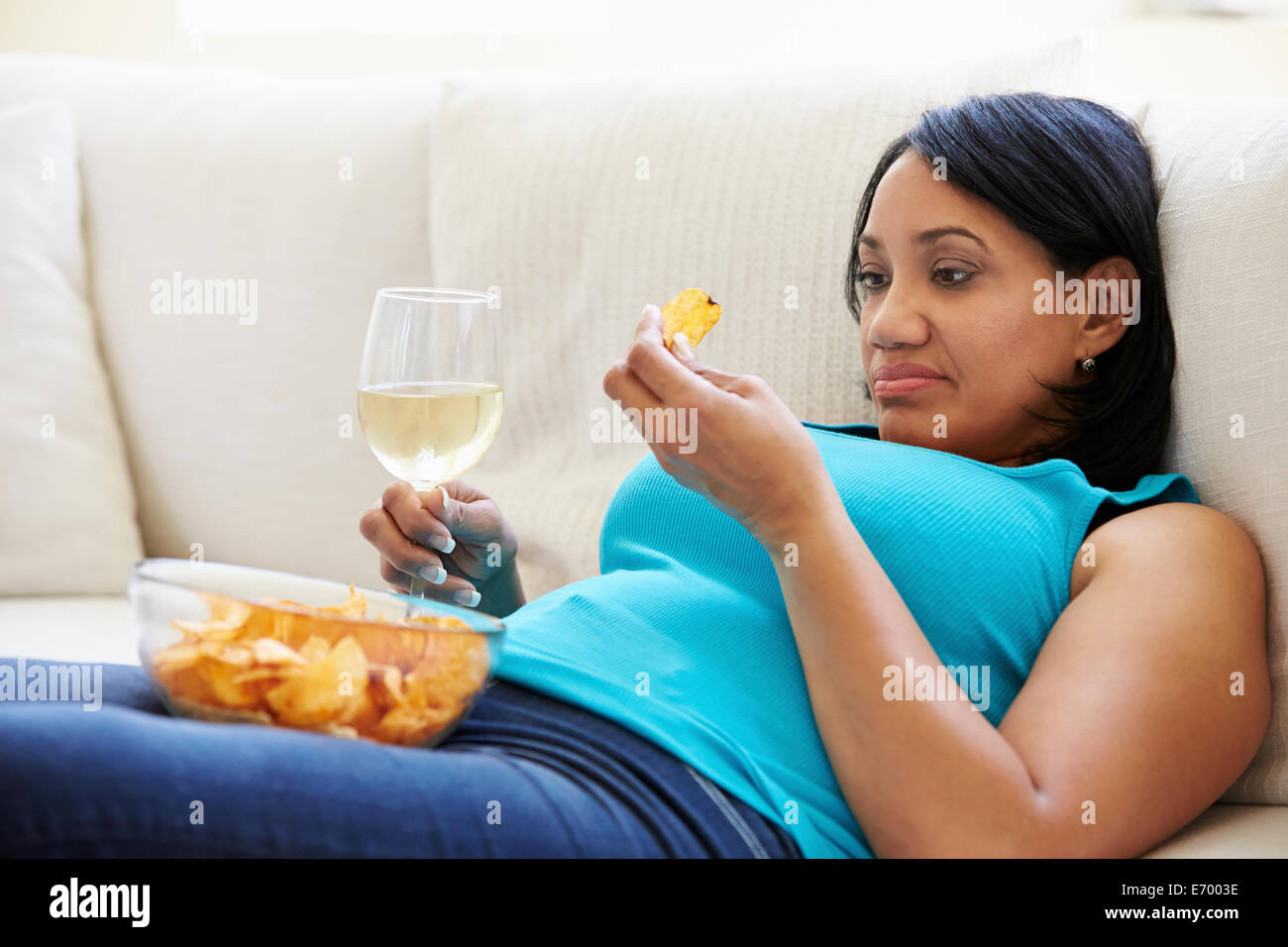 Übergewichtige Frau zu Hause essen Chips und trinken Wein Stockfoto