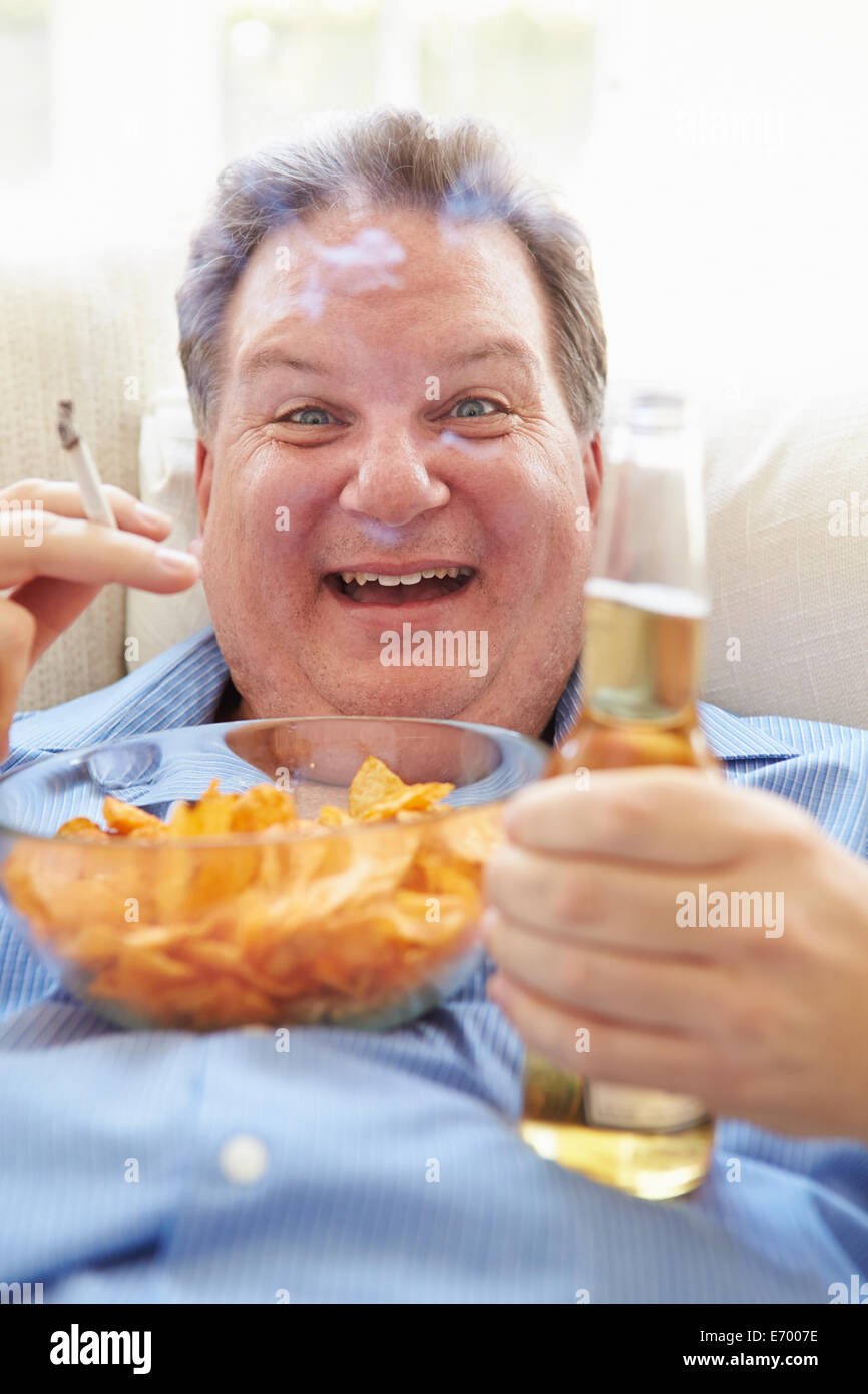 Übergewichtige Menschen essen Chips, Bier trinken und Rauchen Stockfoto