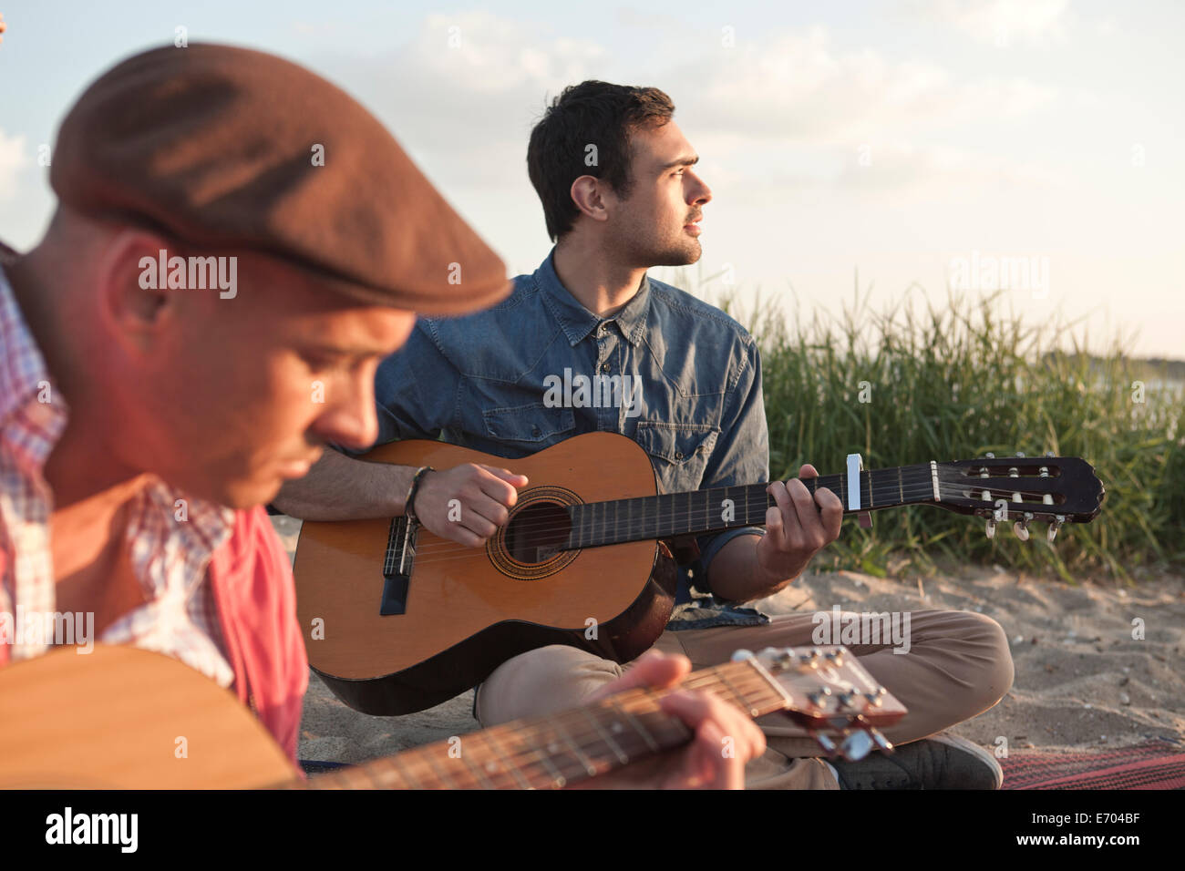 Zwei erwachsenen männlichen Freunden spielen akustische Gitarren am Strand von Bournemouth, Dorset, Großbritannien Stockfoto
