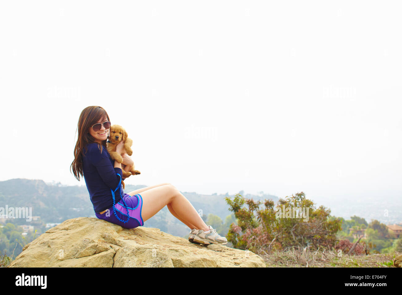Junge Frau sitzt auf Felsen, mit Labrador-Welpe Stockfoto