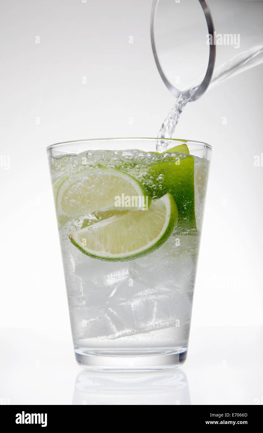 Klarem Wasser eingießen von Krug in Trinkglas mit Kalk und Eiswürfeln Stockfoto