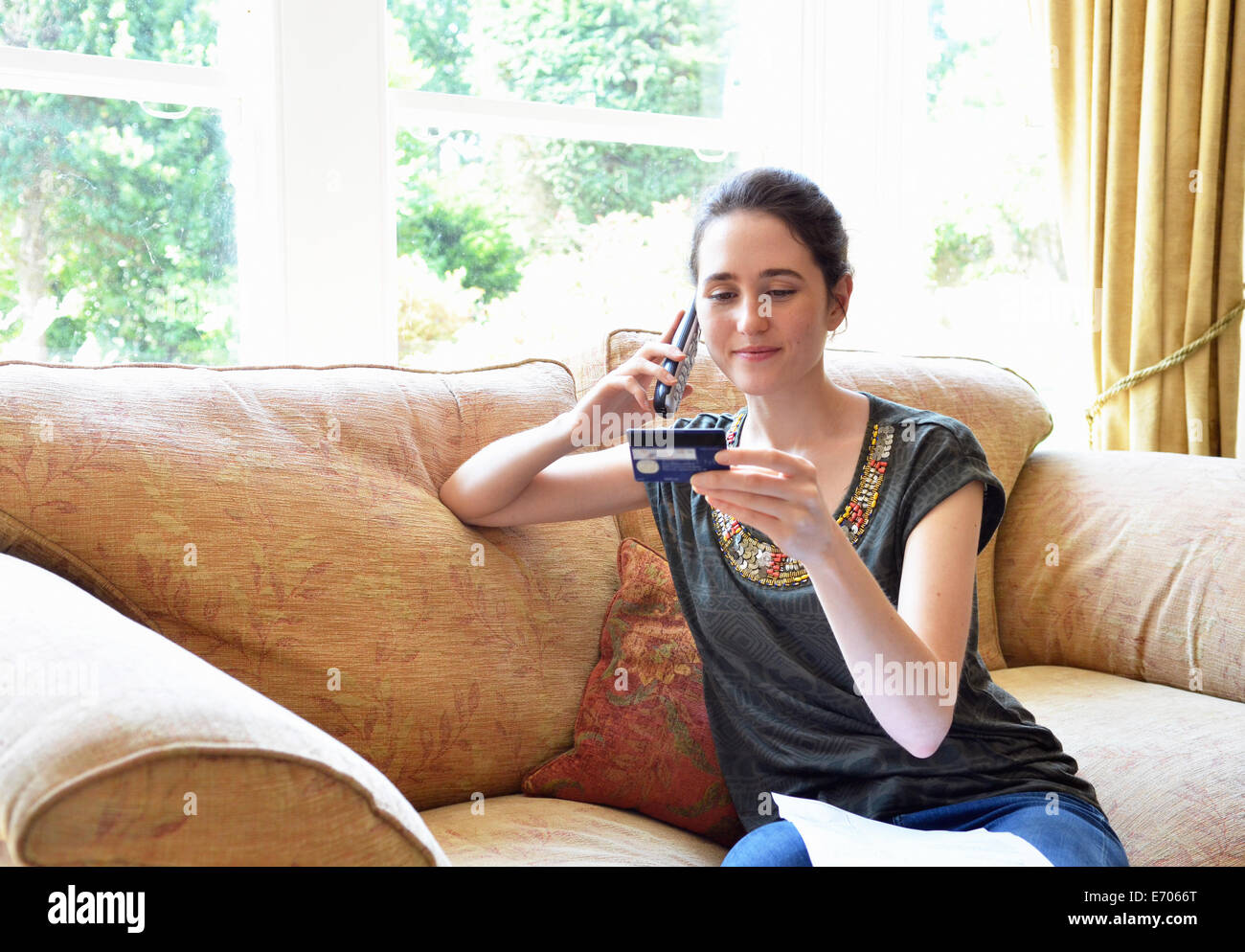 Junge Frau sitzt auf dem Sofa zu Hause einkaufen auf Festnetz-Telefon Stockfoto
