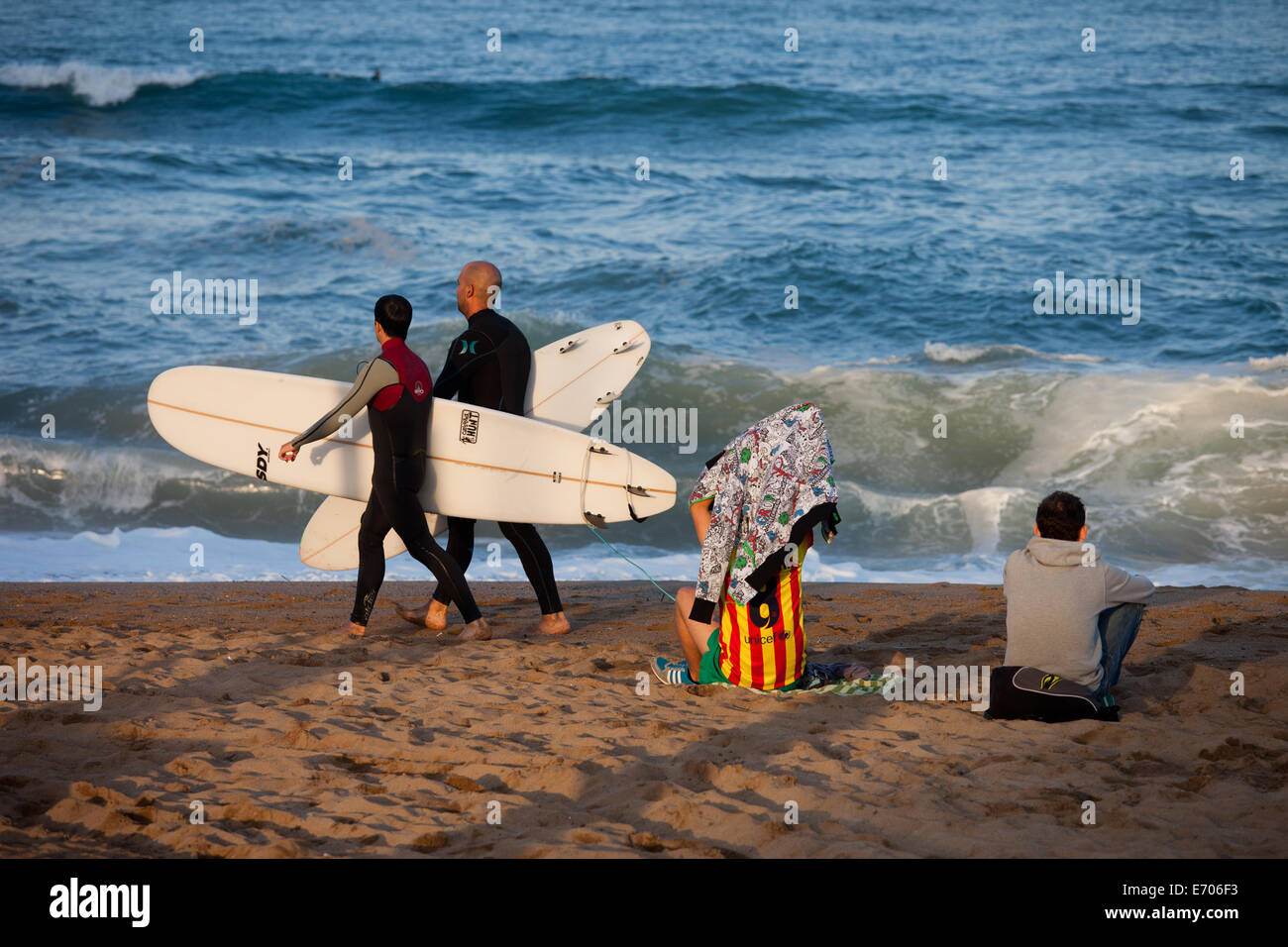 Surfer gehen mit Surfbrettern, sitzt FC Barcelona Fan mit einem Freund am Strand von Barceloneta in Barcelona, Katalonien, Spanien. Stockfoto