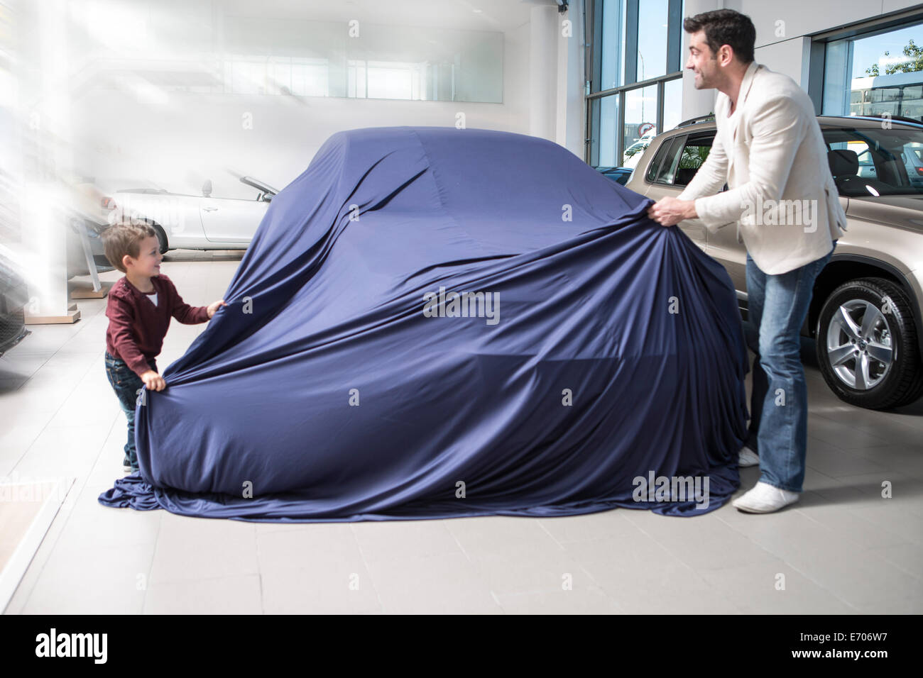 Mitte erwachsenen Mannes aufdecken Neuwagen mit Sohn im Autohaus Stockfoto