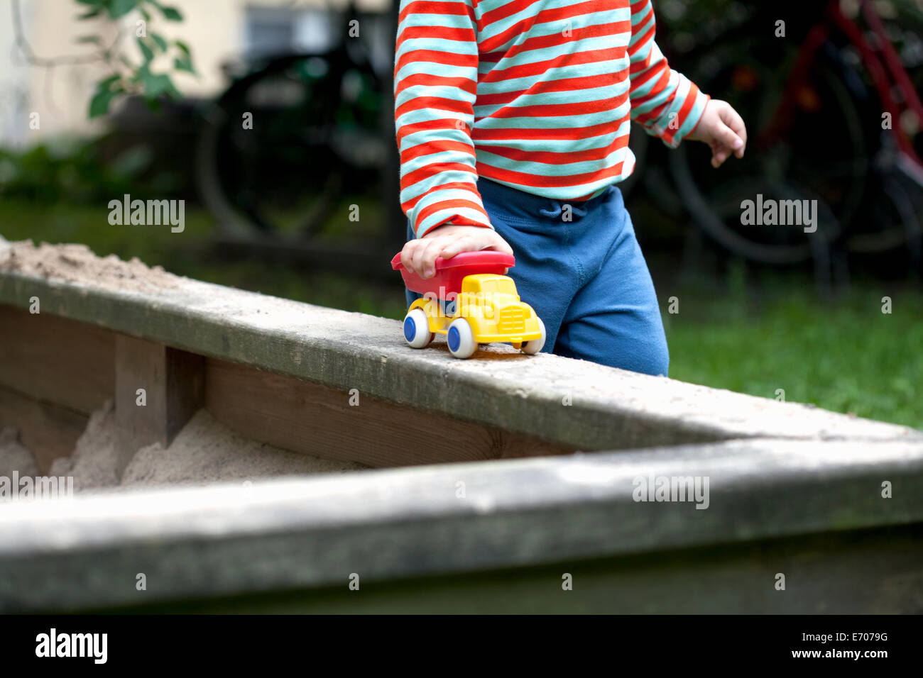 Schuss von männlichen Kleinkind drängen Spielzeugauto herum Sandkasten im Garten beschnitten Stockfoto