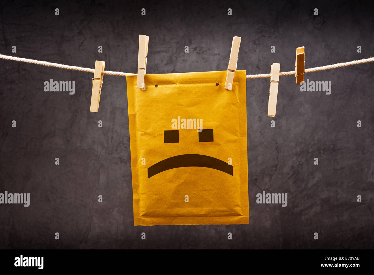 Trauriges Gesicht Emoticon auf Postal Mail, den Umschlag am Seil hängend befestigt mit Kleidung Stifte. Schlechte Nachrichten-Konzept. Stockfoto