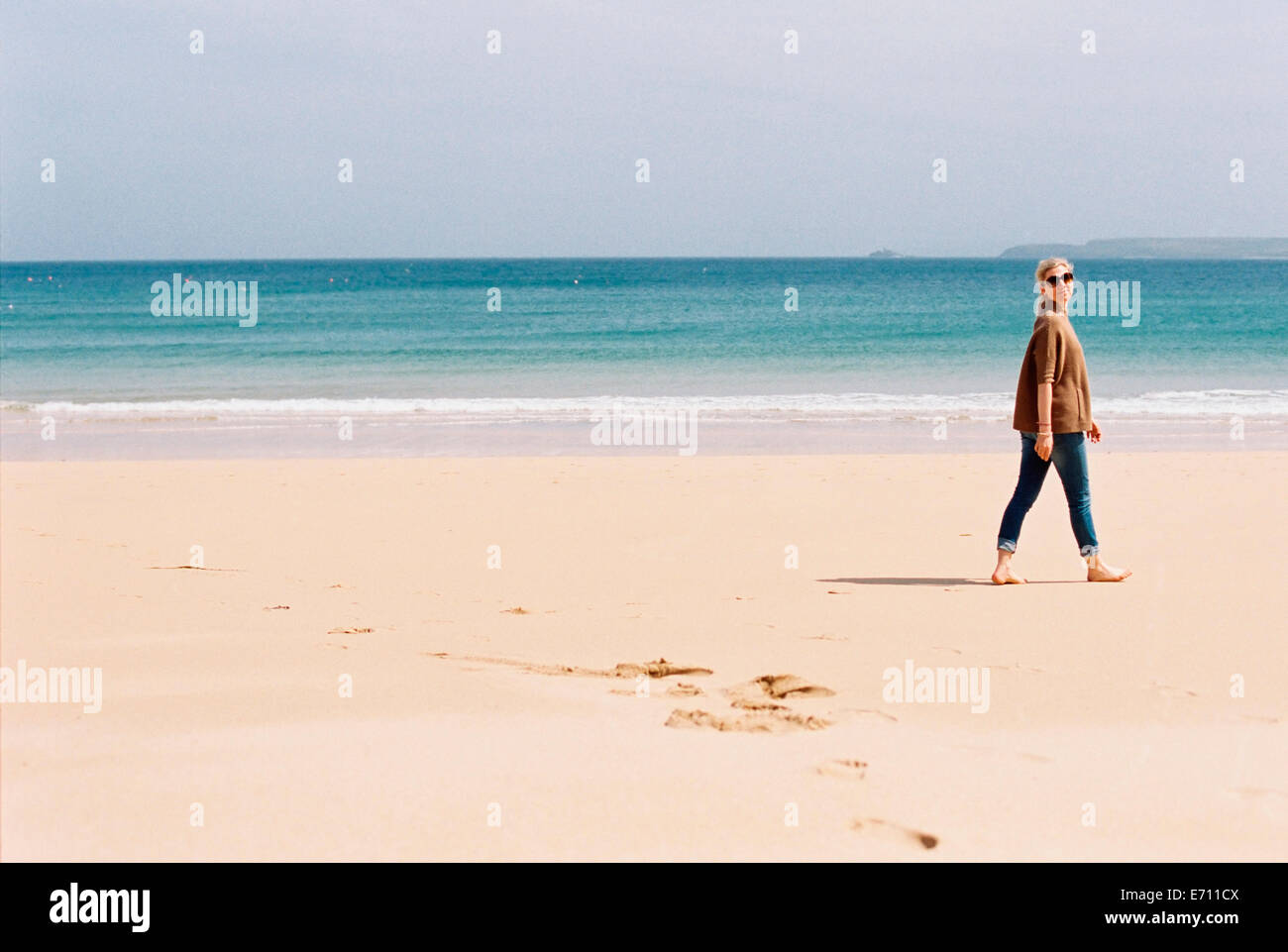 Eine Frau barfuss am Strand, so dass Fußspuren im Sand. Stockfoto