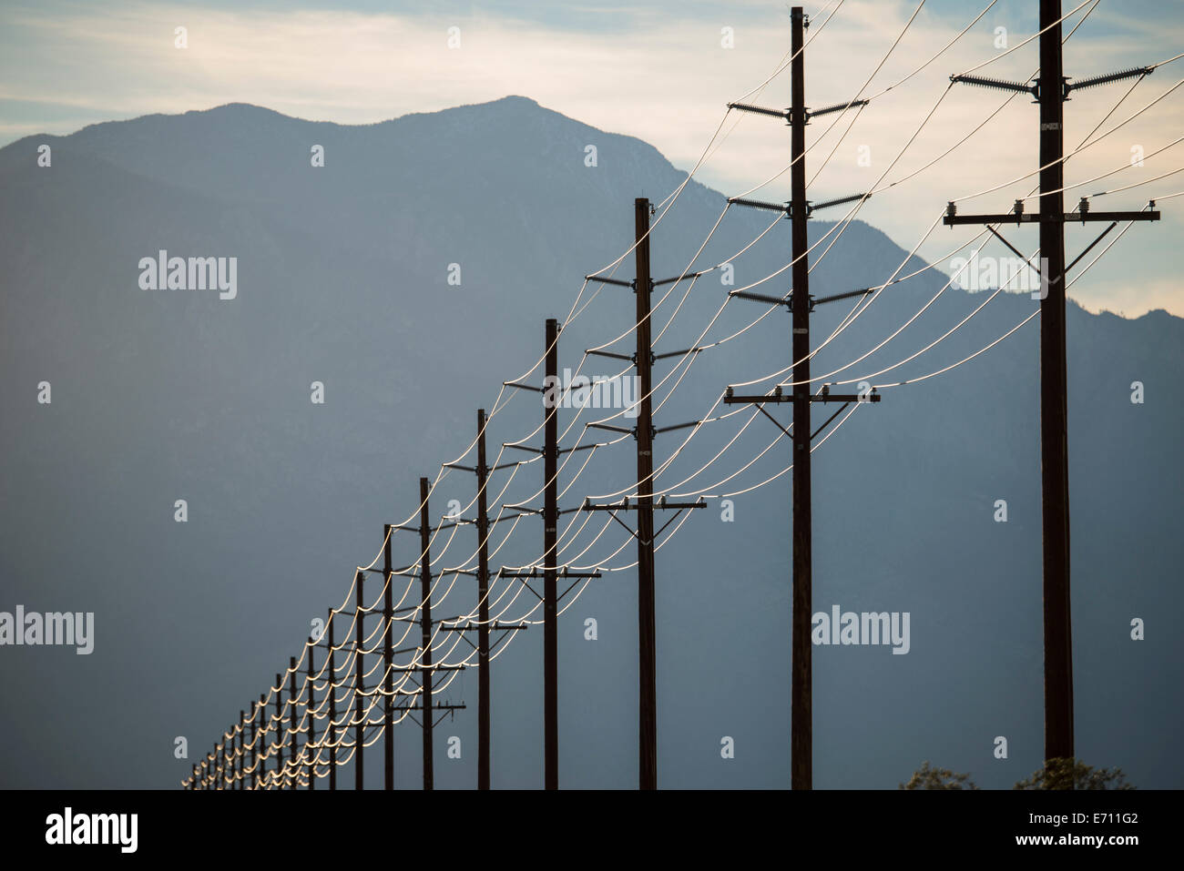 Stromleitungen in Reihen über die Landschaft vor einem Berg und Sonnenuntergang Himmel. Stockfoto