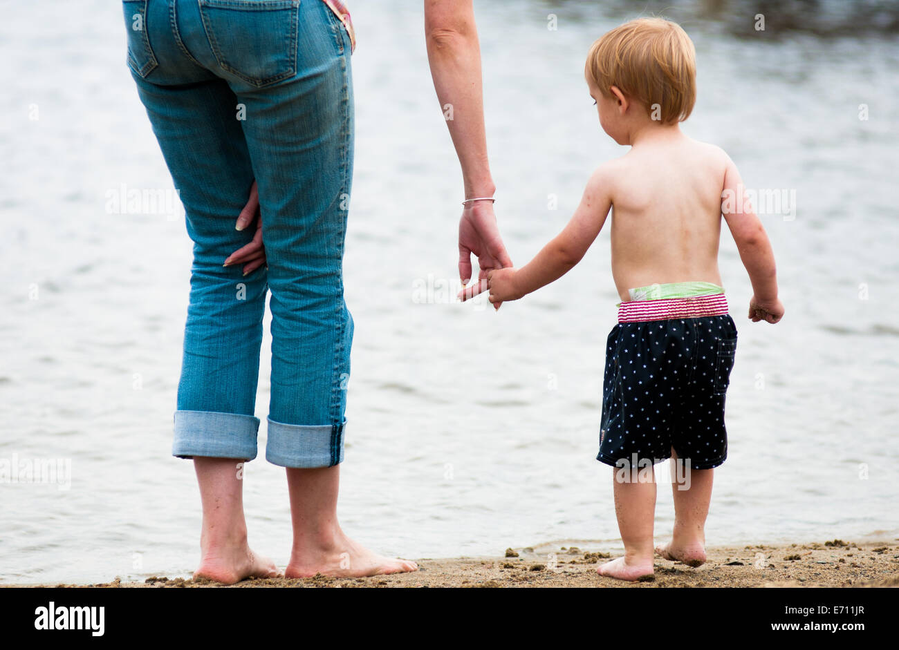 Eine Mutter hält ihr Kleinkind Sohn Hand, wie sie am Strand Fuß. Stockfoto