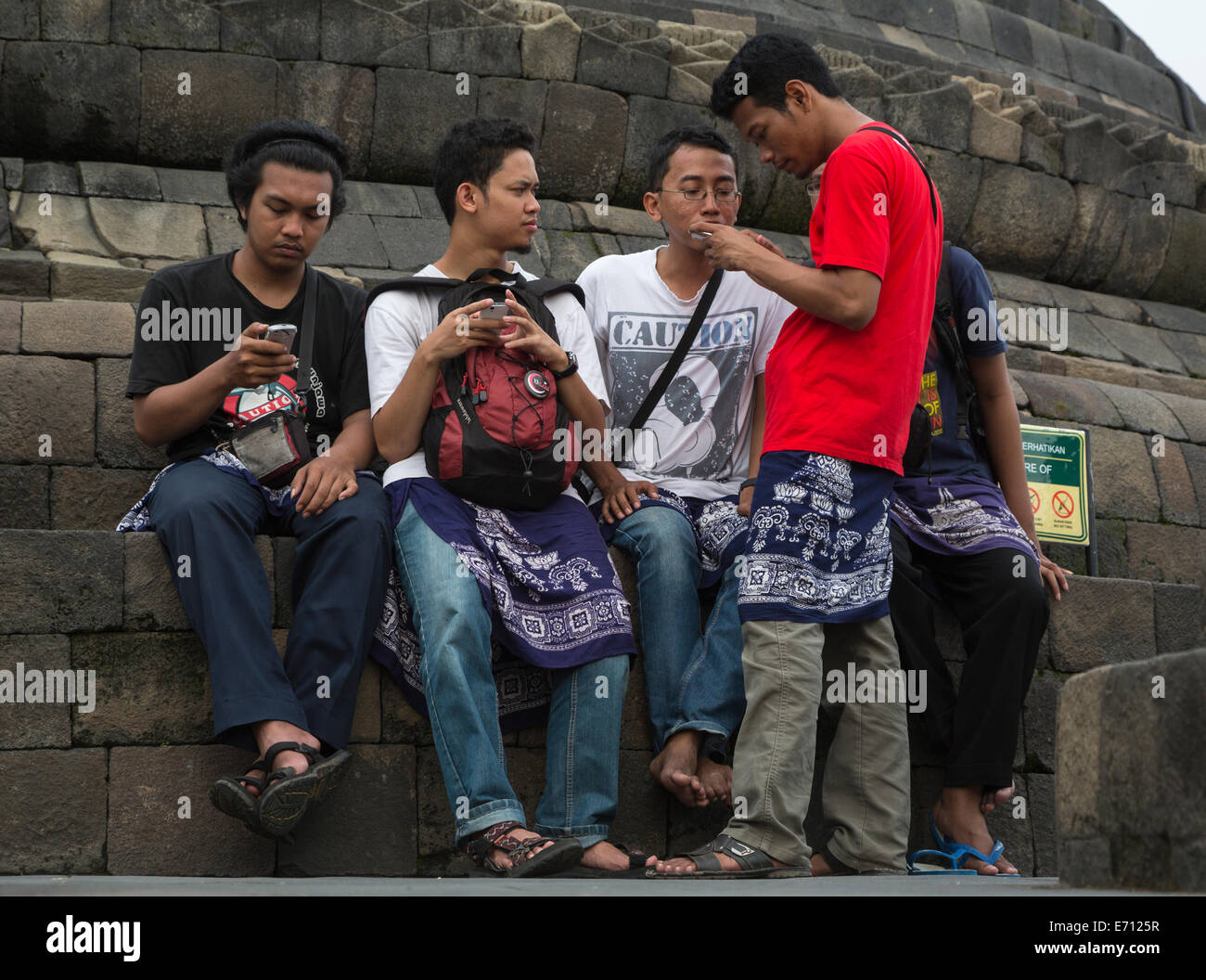 Borobudur, Java, Indonesien.  Junge indonesische Männer überprüfen ihre Handys während des Besuchs des Tempels. Stockfoto