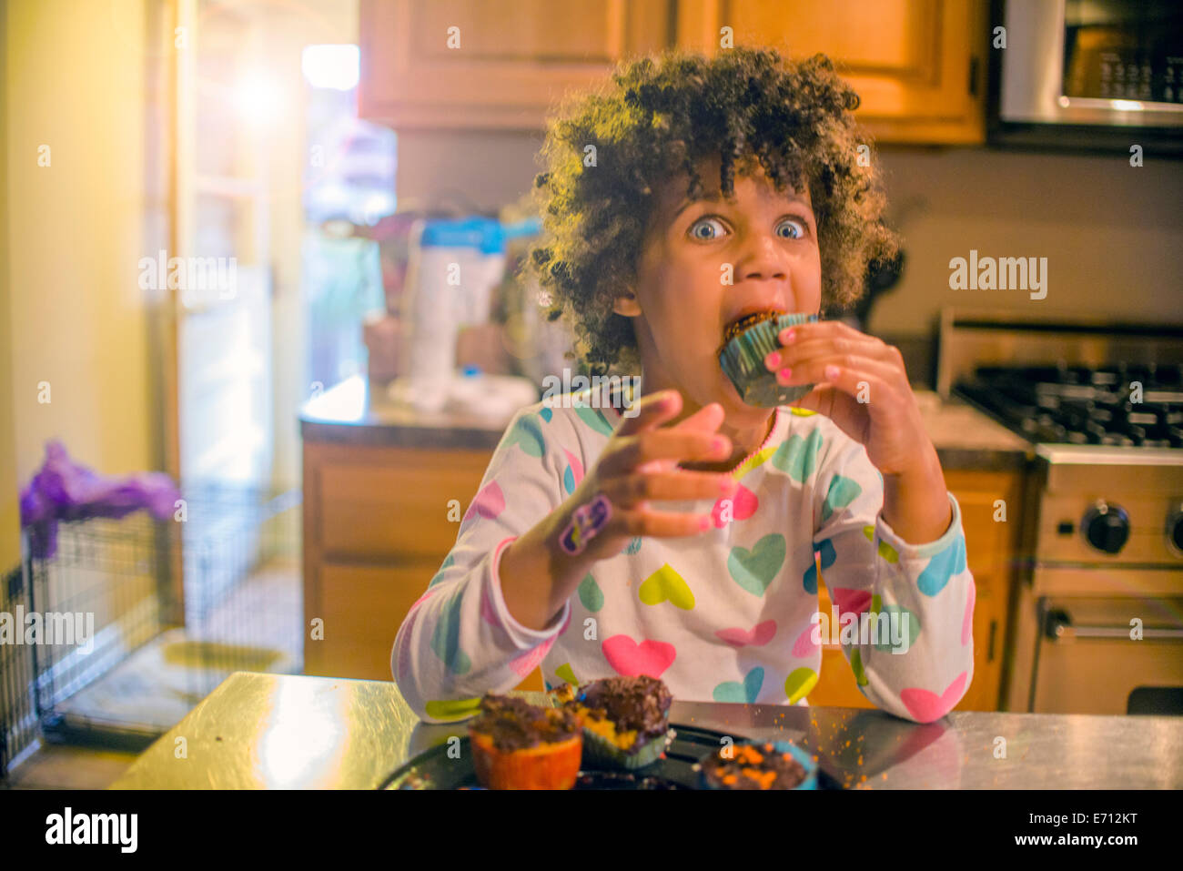 Porträt von überrascht Mädchen essen Muffins am Küchentisch Stockfoto