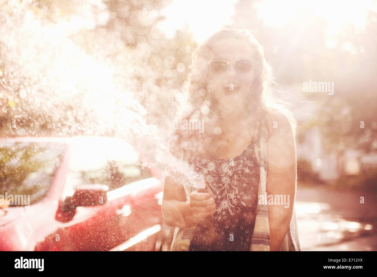 Junge Frau Besprühen mit Wasser aus Gartenschlauch Stockfoto