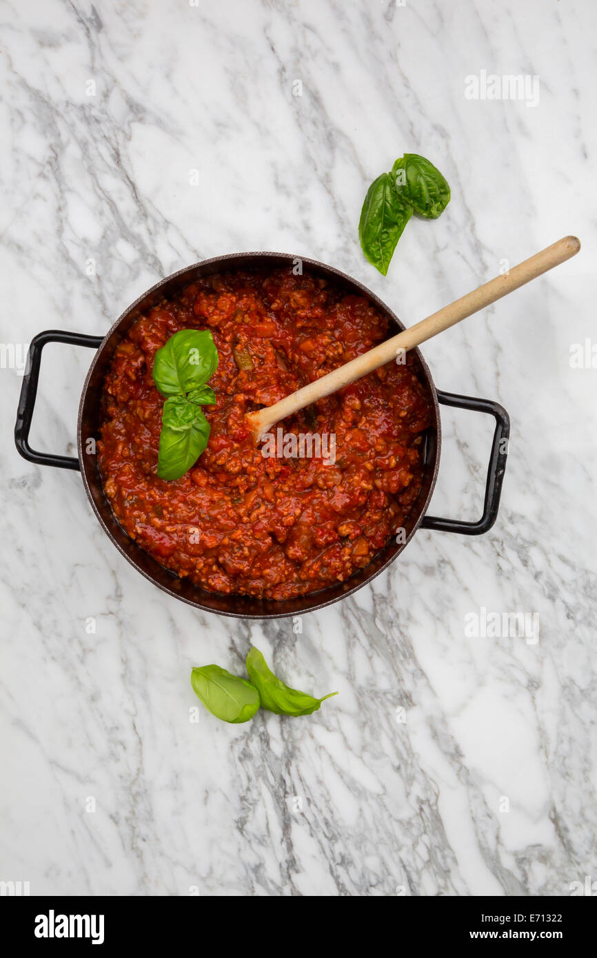 Kochtopf der Bolognese-Sauce und Basilikum Blätter auf weißem Marmor, erhöhten Blick Stockfoto
