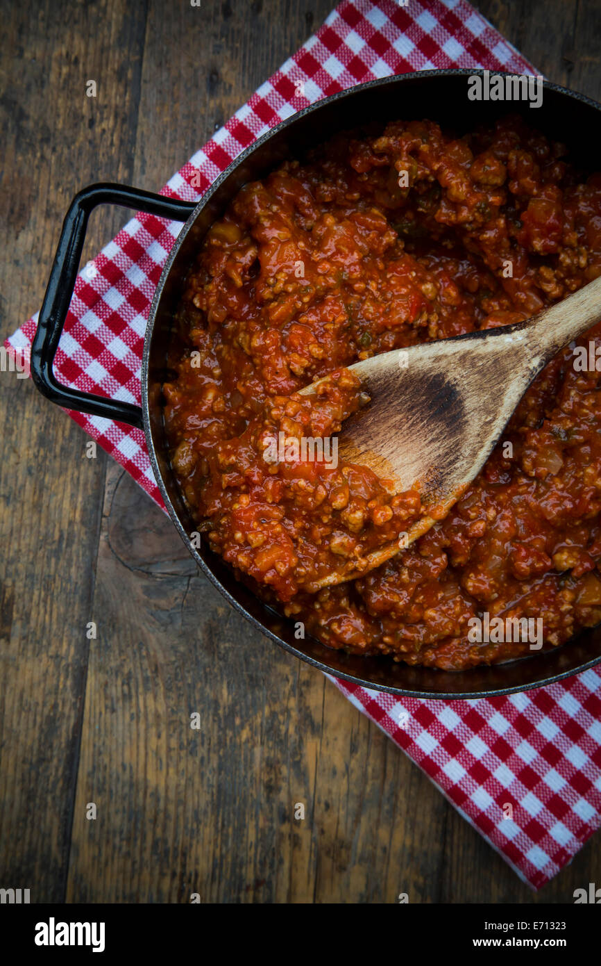 Kochtopf der Bolognese-Sauce mit einem Holzlöffel auf Tuch und dunklem Holz, erhöhten Blick Stockfoto