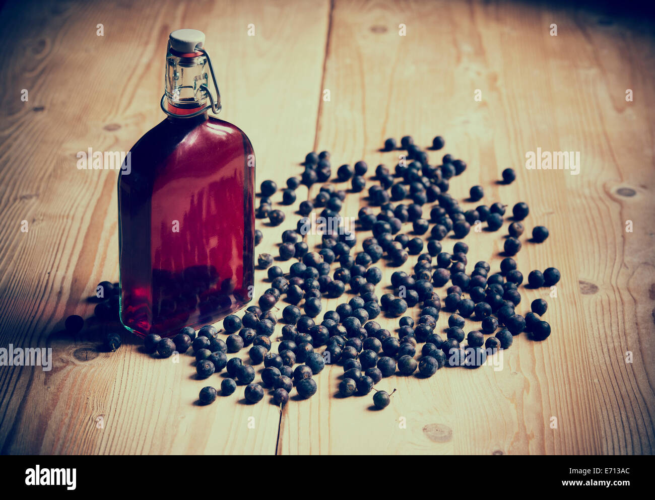 Prunus Spinosa. Blackthorn / Schlehe Beeren und eine Flasche Schlehe gin auf einem hölzernen Küchentisch. Retro-Vintage-Stil Stockfoto