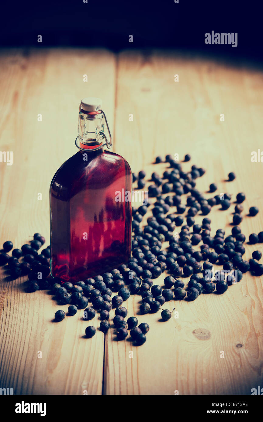 Prunus Spinosa. Blackthorn / Schlehe Beeren und eine Flasche Schlehe gin auf einem hölzernen Küchentisch. Retro-Vintage-Stil Stockfoto