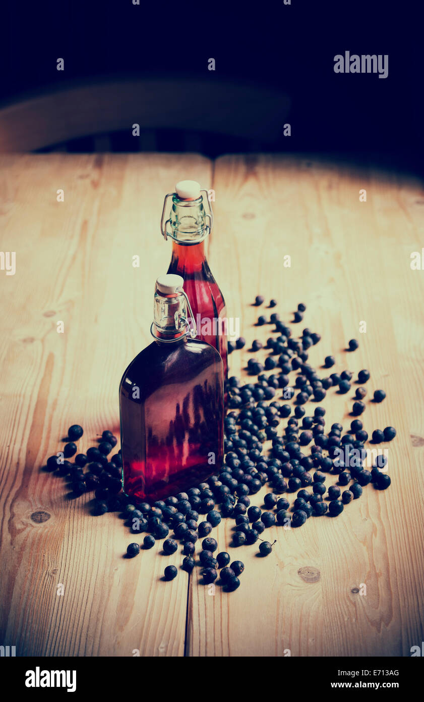 Prunus Spinosa. Blackthorn / Schlehe Beeren und zwei Flaschen Schlehe gin auf einem hölzernen Küchentisch. Retro-Vintage-Stil Stockfoto
