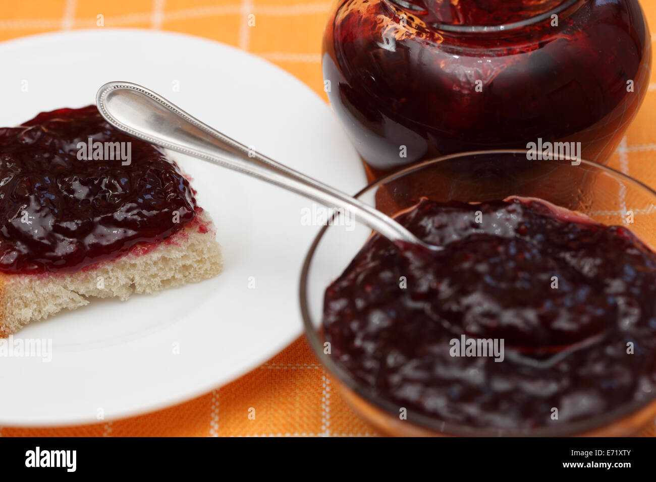 Scheibe Brot mit Marmelade auf einem Teller, Glas und Glas Schüssel mit Marmelade mit Tee-Löffel. Closeup. Stockfoto