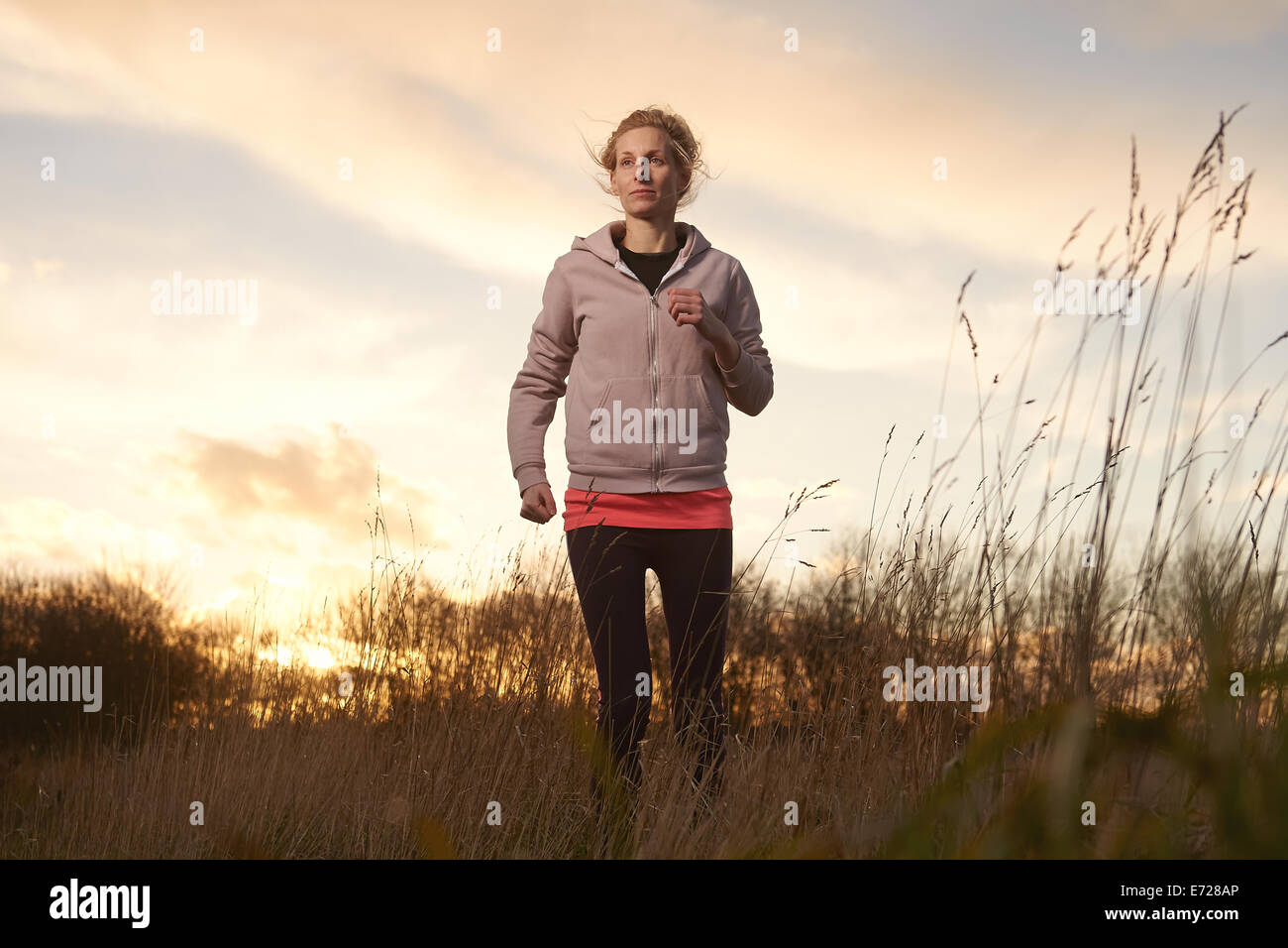 Eine Frau in ihr 30 läuft in einem Feld lange Gras als die Sonne untergeht Stockfoto