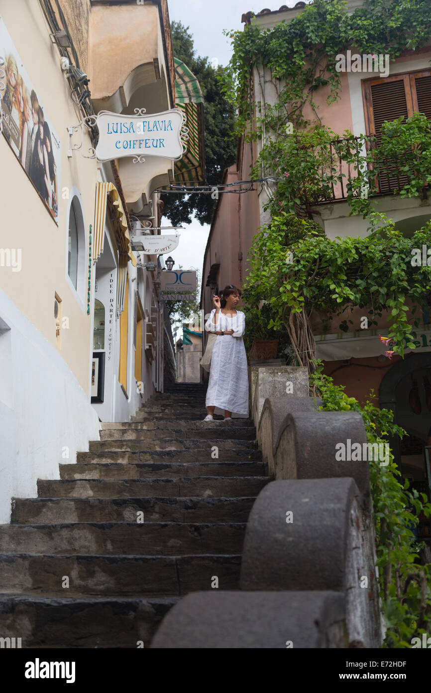 Eine Frau steht nachdenklich mit Blick auf Touristen auf der Treppe vor ihrem Geschäft in der ziemlich italienischen Stadt Positano zu rauchen Stockfoto