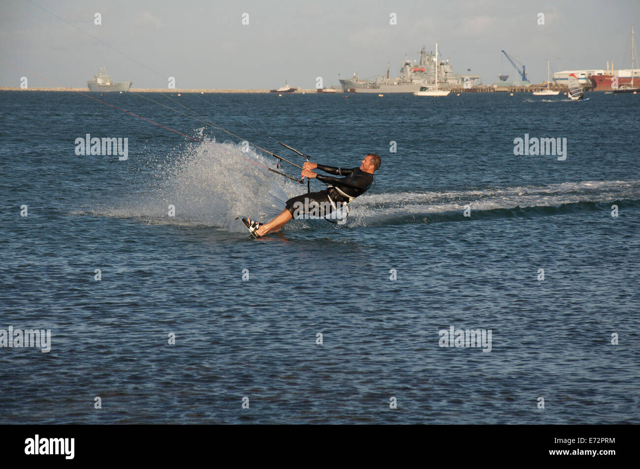 Wassersport. Männliche Kiteboarder, das Tragen von Neoprenanzug, über das Wasser des Portland Harbour in Dorset, England, Vereinigtes Königreich. Stockfoto