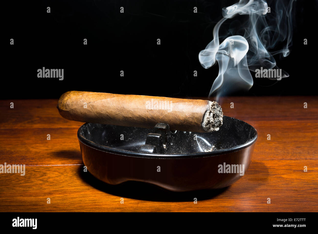 Eine brennende Zigarre in einem klassischen schwarzen Aschenbecher Streaming-Rauchen in einem dunklen, stimmungsvolle Ambiente. Stockfoto