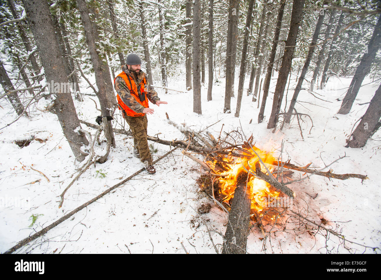 Ein männlicher Jäger bleibt neben einem Feuer im Schnee warm. Stockfoto