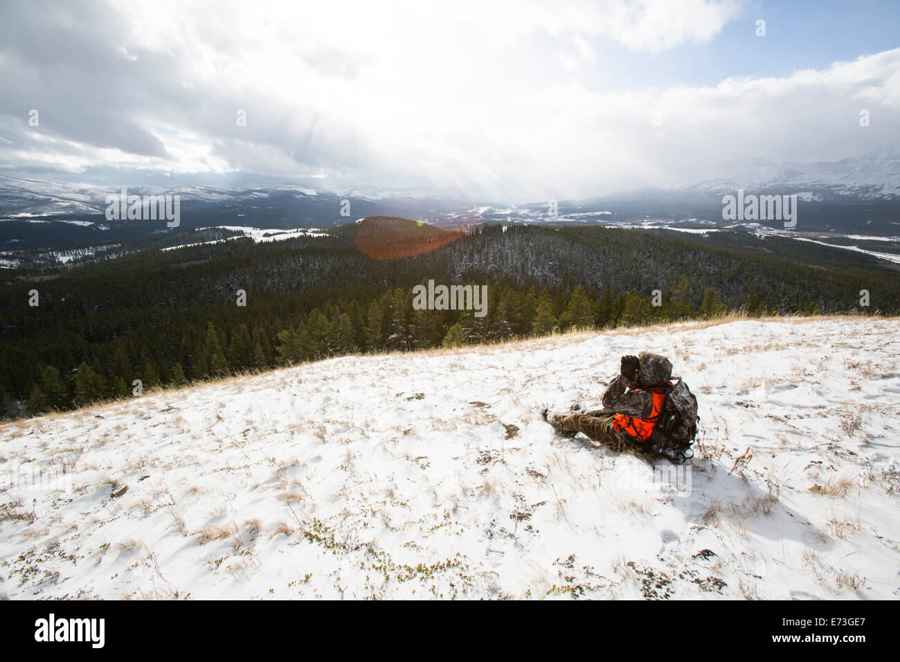 Ein männlicher Jäger schaut durch ein Fernglas im Schnee. Stockfoto