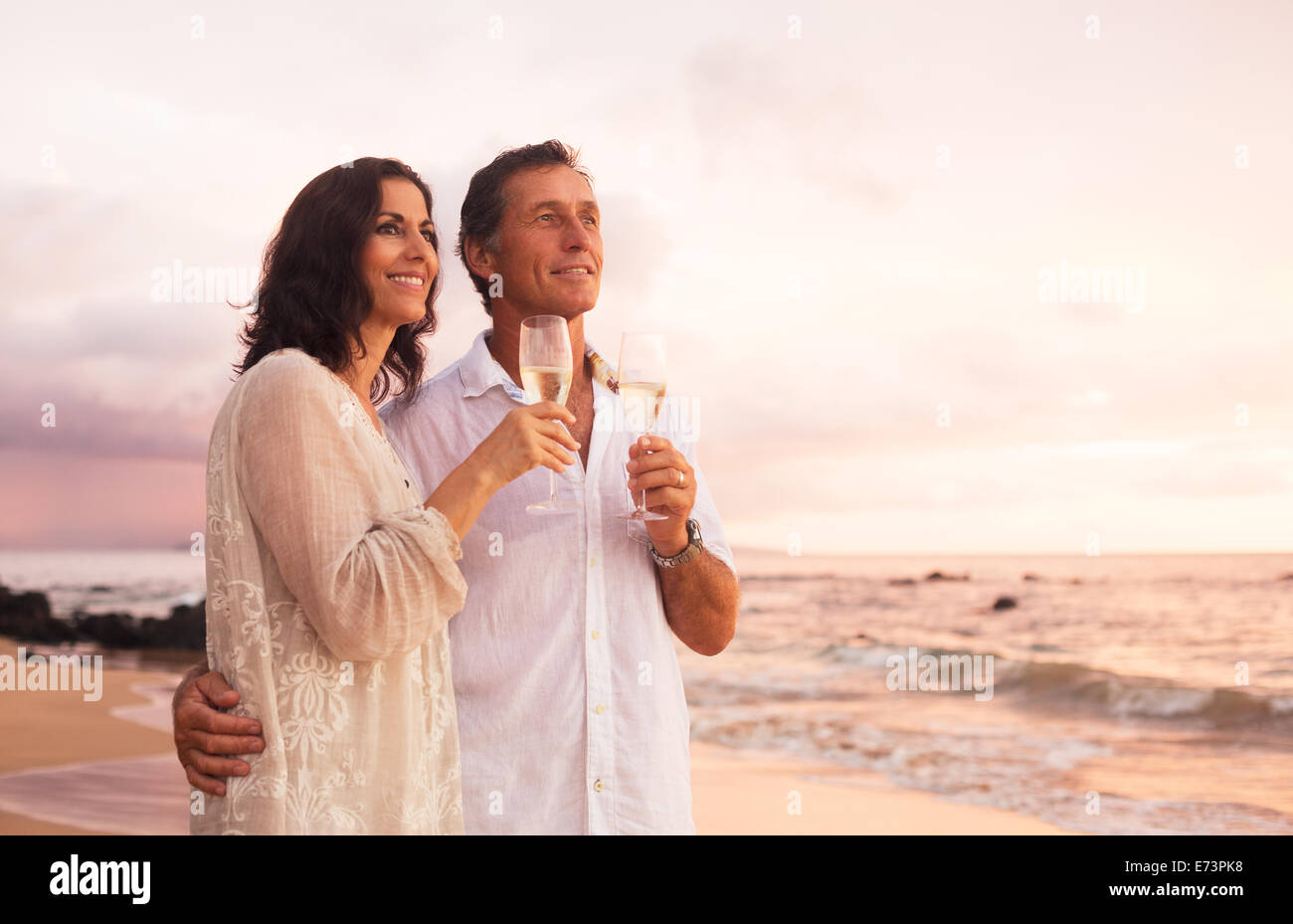 Romantische Reife Brautpaar Champagner trinken am Strand bei Sonnenuntergang. Urlaub-Reisen-Ruhestand-Jahr-Feier. Stockfoto