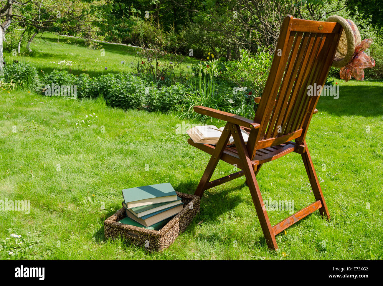 hölzerne Relaxsessel, Bücher in Korb und Hut im Garten Garten im Sommertag. Stockfoto