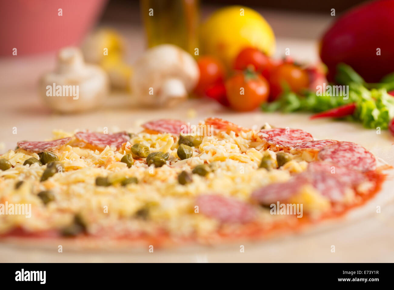 rohe italienische Salami Pizza am Tisch mit Zutaten Stockfoto