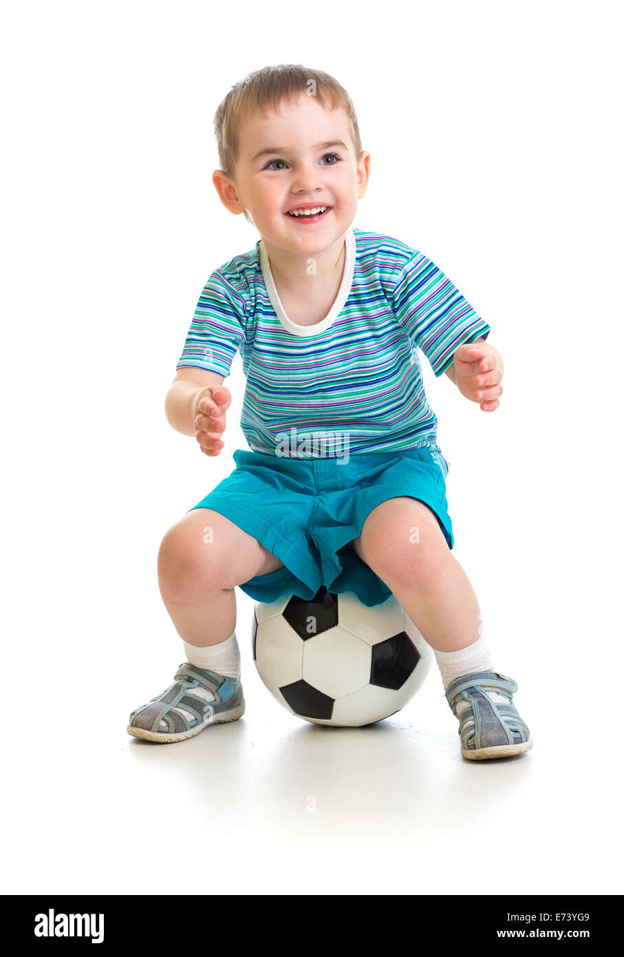Kleiner Junge sitzt auf Fußball isoliert auf weiss Stockfoto