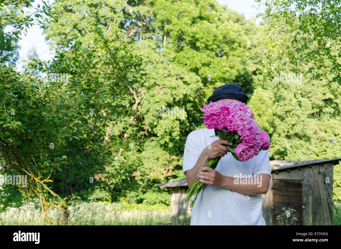 Mann versteckt sein Gesicht mit großen rosa Pfingstrose Bouquet von Frühlingsgarten Stockfoto