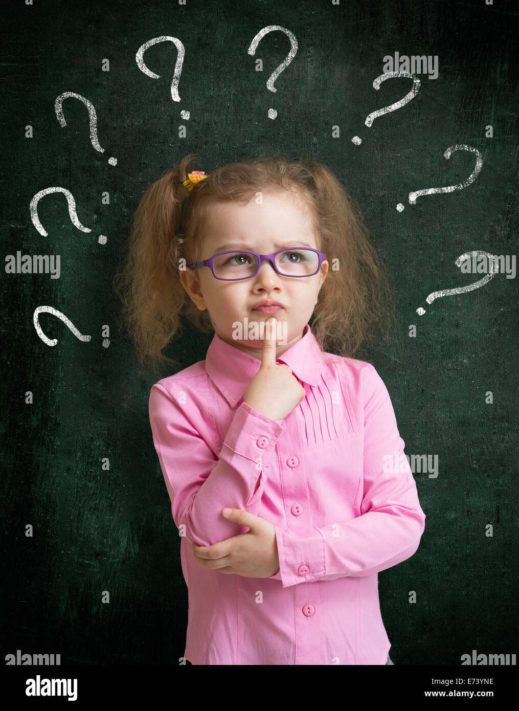 Kind in Brillen stehen in der Nähe von Schultafel mit vielen Fragezeichen Stockfoto