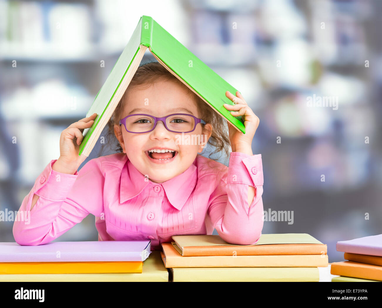Kleines Mädchen in Gläsern unter Dach aus Buch gemacht. Stockfoto