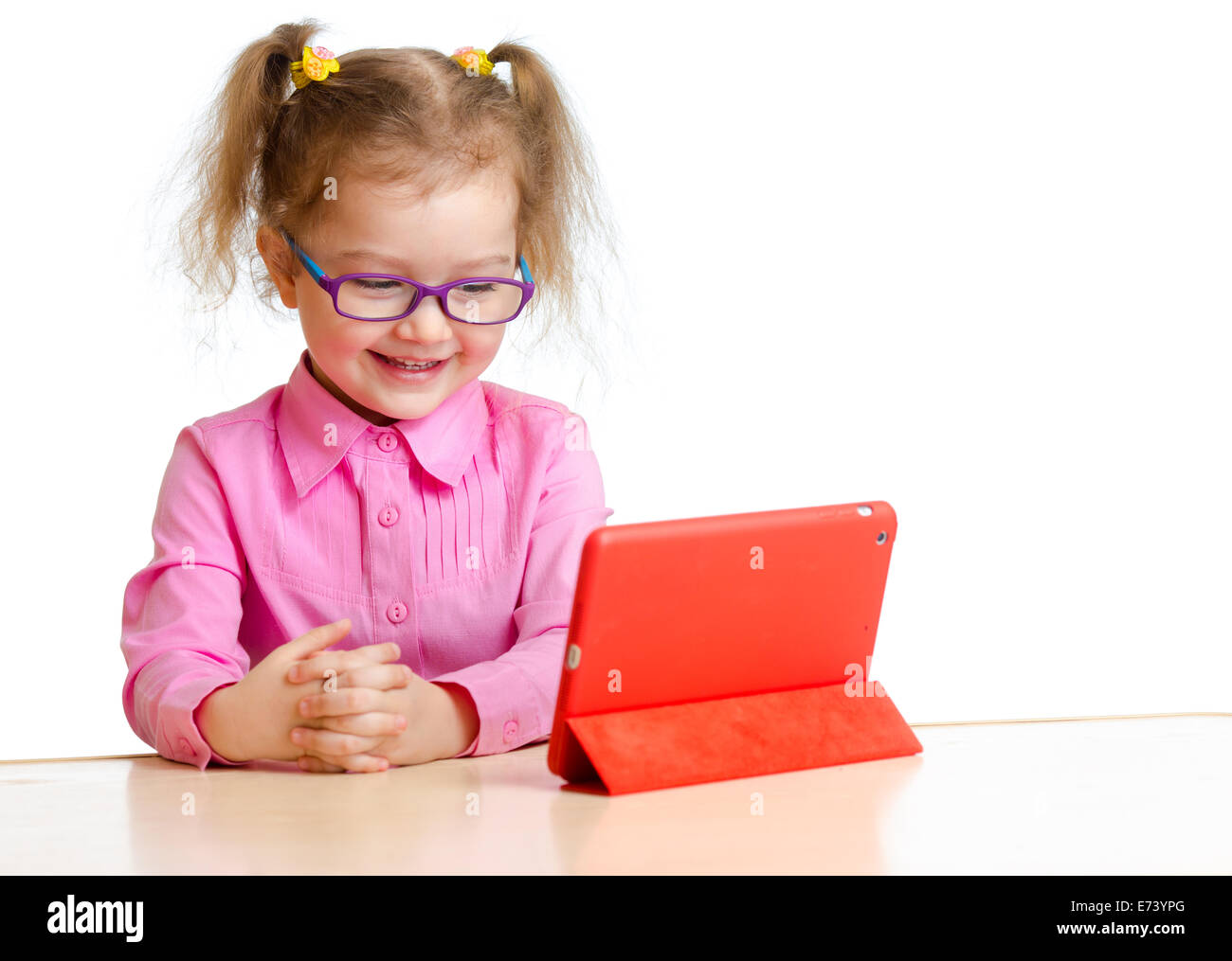 lächelndes Kind in Gläser Blick auf Mini-Tablet-pc-Bildschirm sitzen am Tisch Stockfoto