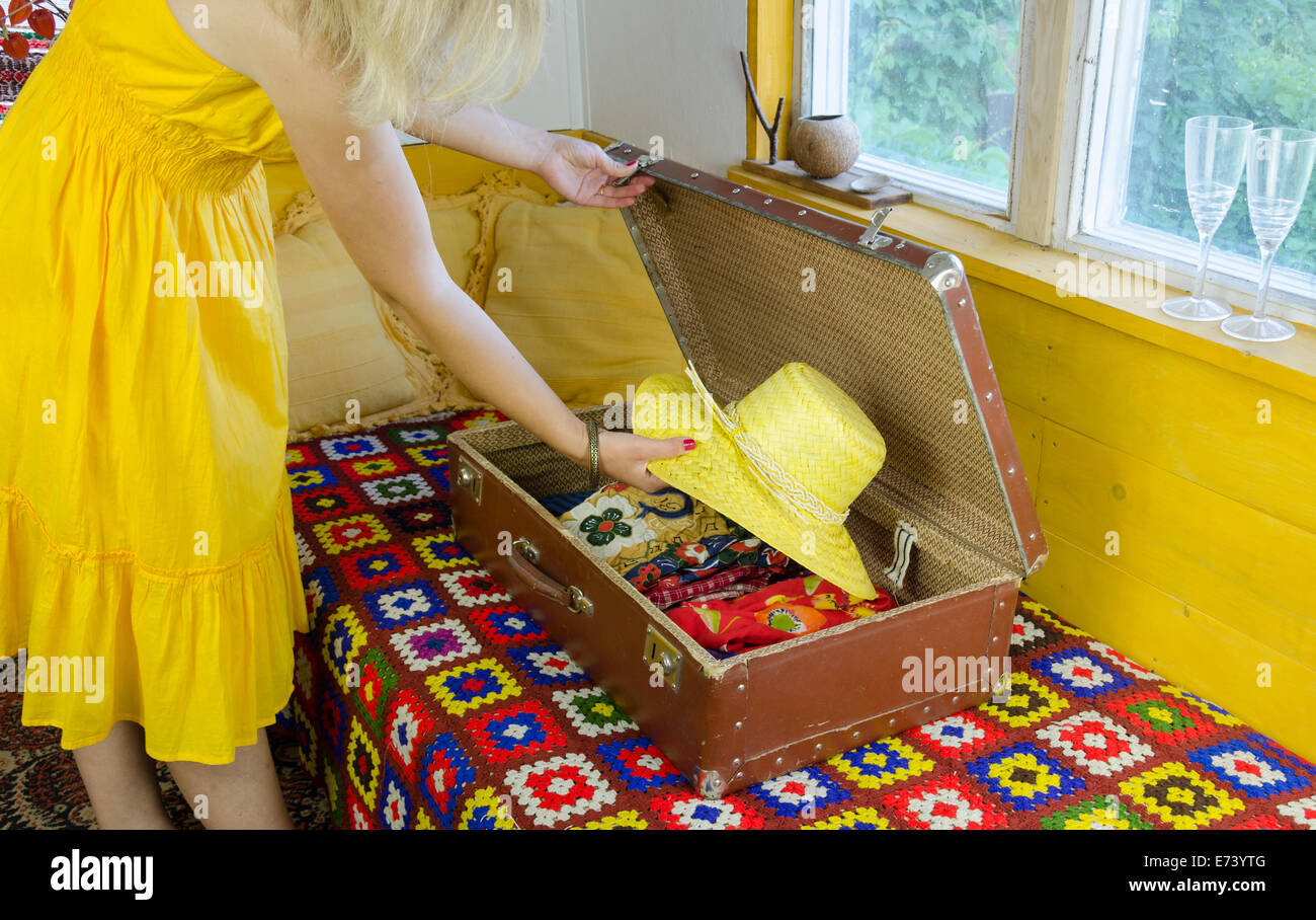 Frau mit gelben Sommerkleid setzen Strohhut in alten Leder-Koffer Stockfoto