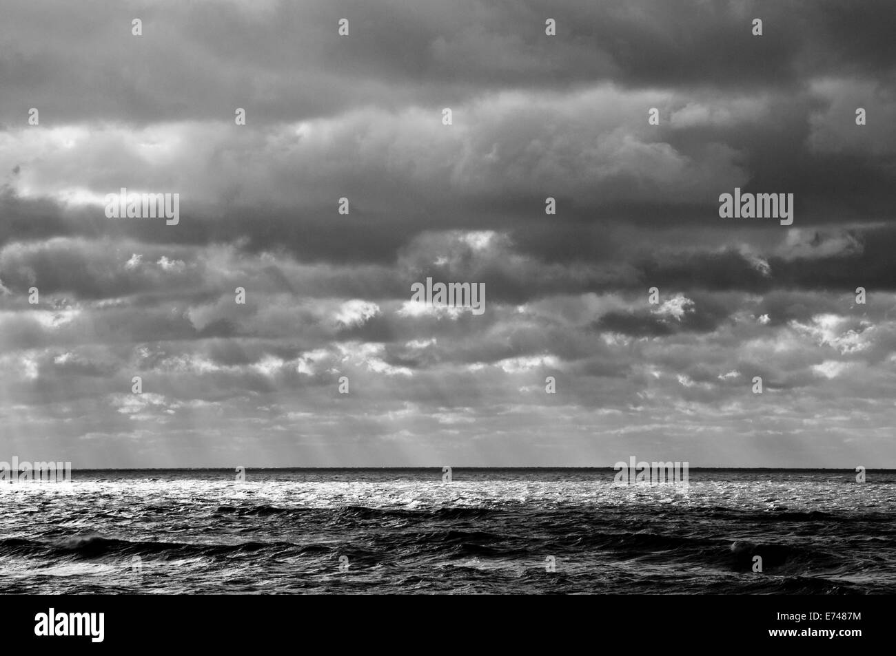 Ein schwarz-weiß Bild von dämmerungsaktiv Strahlen piercing einen bewölkten Himmel und Teile des Meeres Leuchten Stockfoto