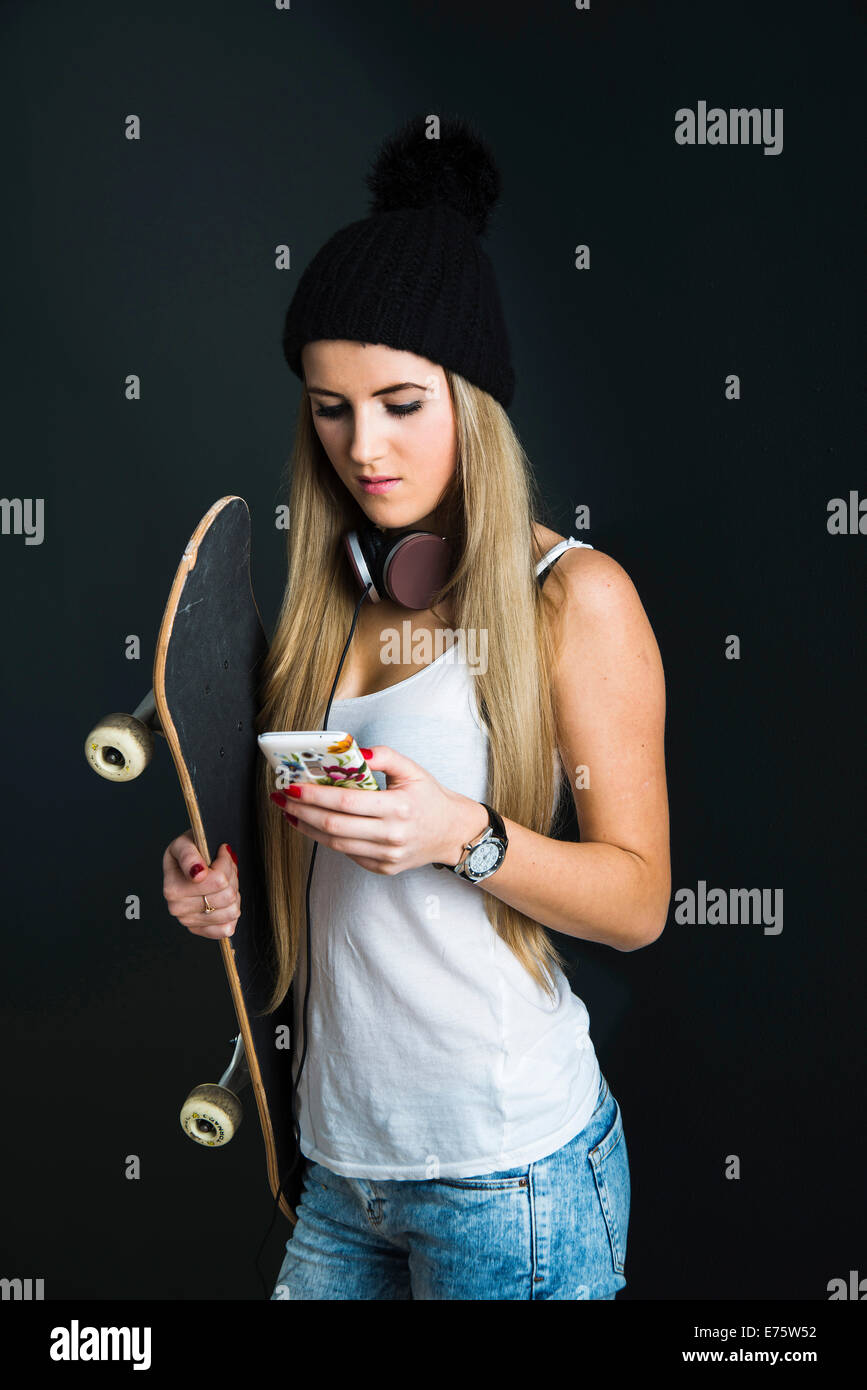 Coole junge Frau mit einem Skateboard, Kopfhörer und ein Handy Stockfoto
