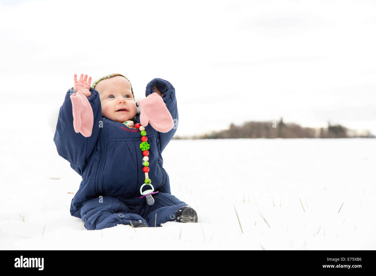 Baby, 9 Monate, sitzt mit einem Schneeanzug im Schnee Stockfoto