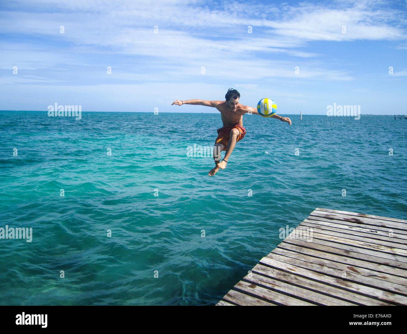 junger Mann springt einem Pier beim treten eines Fußballs Bilder aus dem Monat in Caye Caulker, Belize Stockfoto