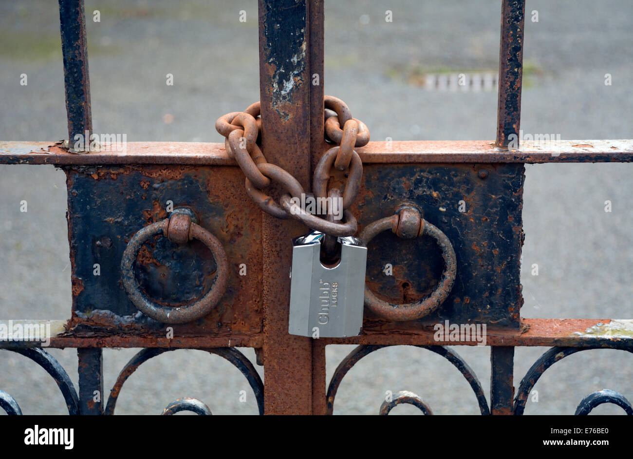 Reich verzierte Tore durch ein neues Schloss auf eine rostige Kette gesichert. Stockfoto