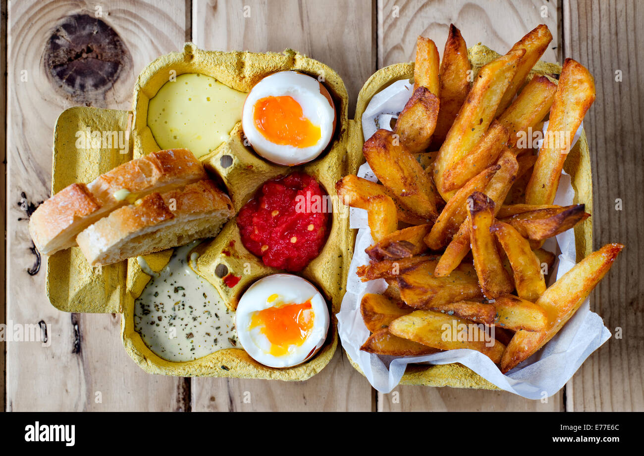 Weich gekochtes Ei mit Pommes Frites und Saucen in einer Kiste Kartonschachtel. Stockfoto