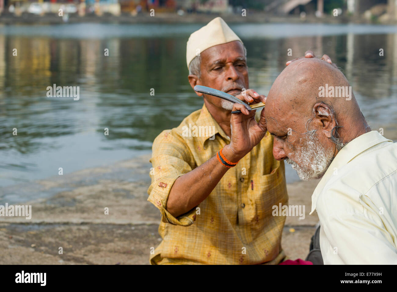 Ein Barbier rasieren ist einen Pilger am Ufer des heiligen Flusses Godwari, Nasik, Maharashtra, Indien Stockfoto