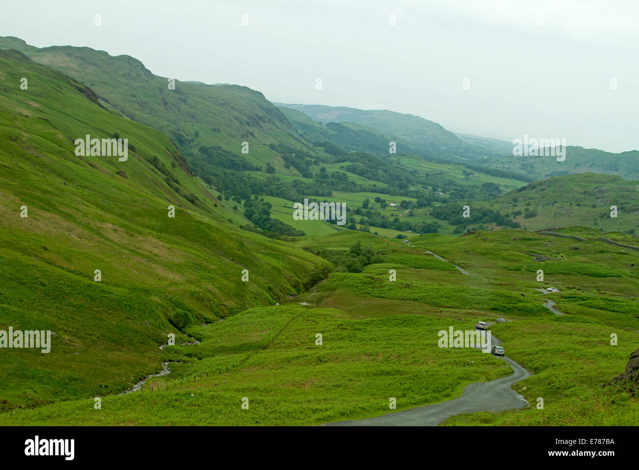 Blick vom Hardknott-Pass, schmale Straße schlängelt sich durch die englische Landschaft der smaragdgrüne Täler, mäandernden Bach, Wälder und Berge des Lake District. Stockfoto