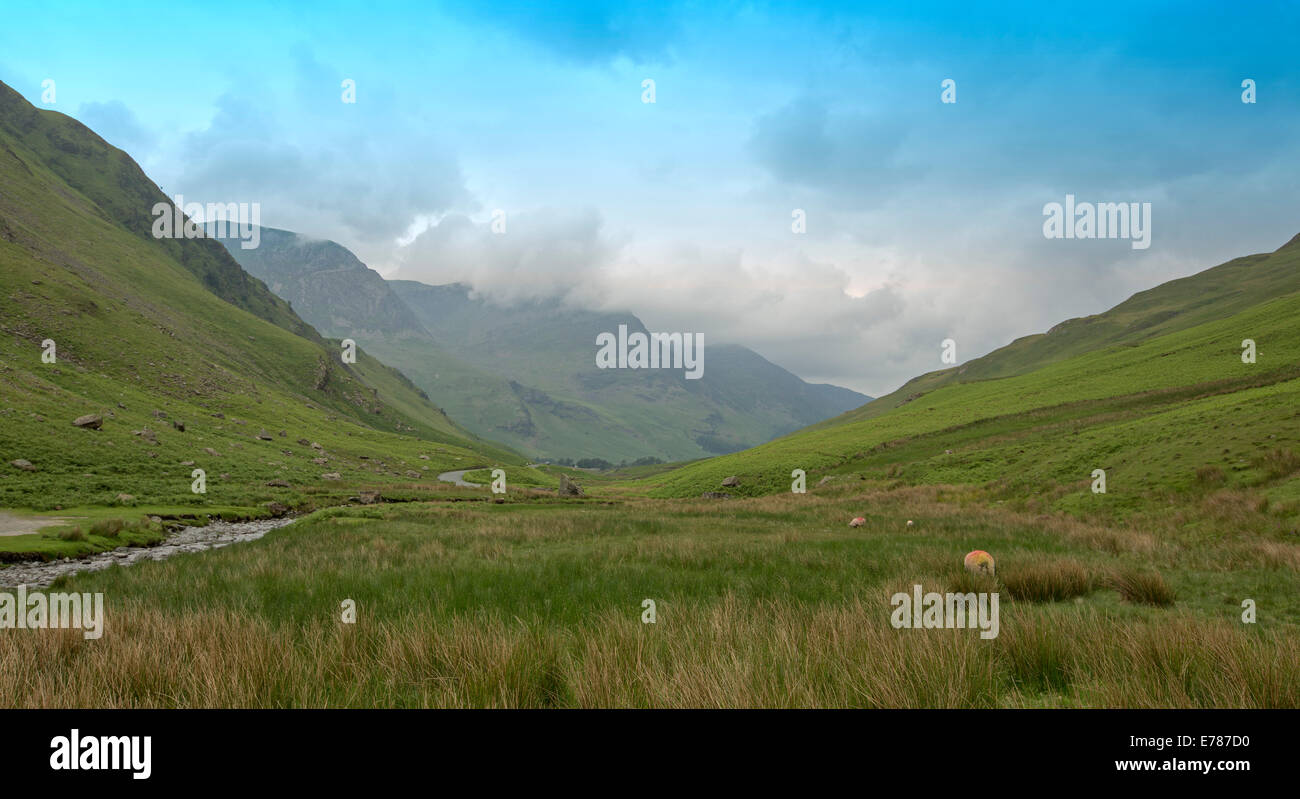 Englische Landschaft bei Honister Pass Cumbria, Smaragd-Tal, murmelte Stream, grünen Hügel und Bergspitzen unter tief hängenden Wolken & blauen Himmel. Stockfoto