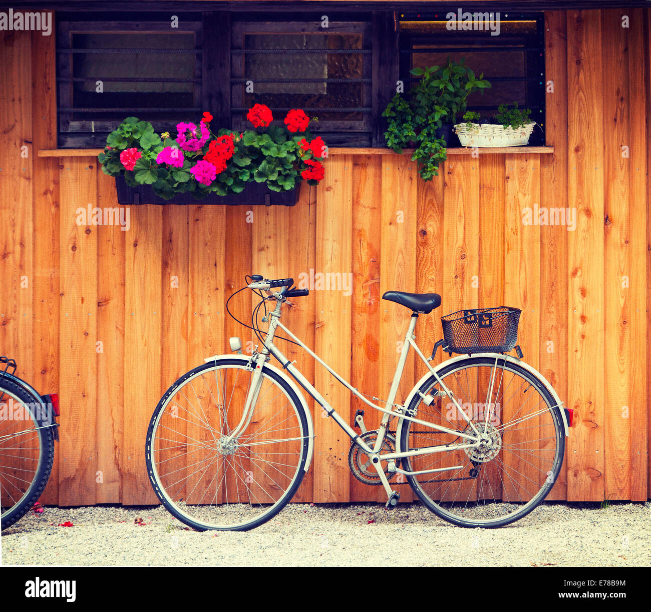 Fahrrad in der Nähe einer Holzhütte mit Geranien und Kräutern Vasen geparkt. Retro-Instagram-Effekt hinzugefügt. Stockfoto