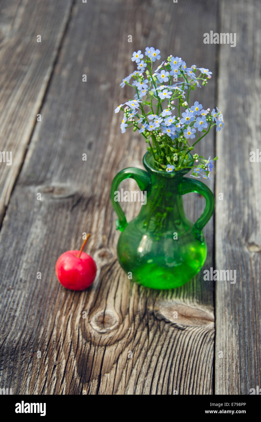 Vergissmeinnicht Blumen in Vase und roter Apfel auf hölzernen Hintergrund Stockfoto